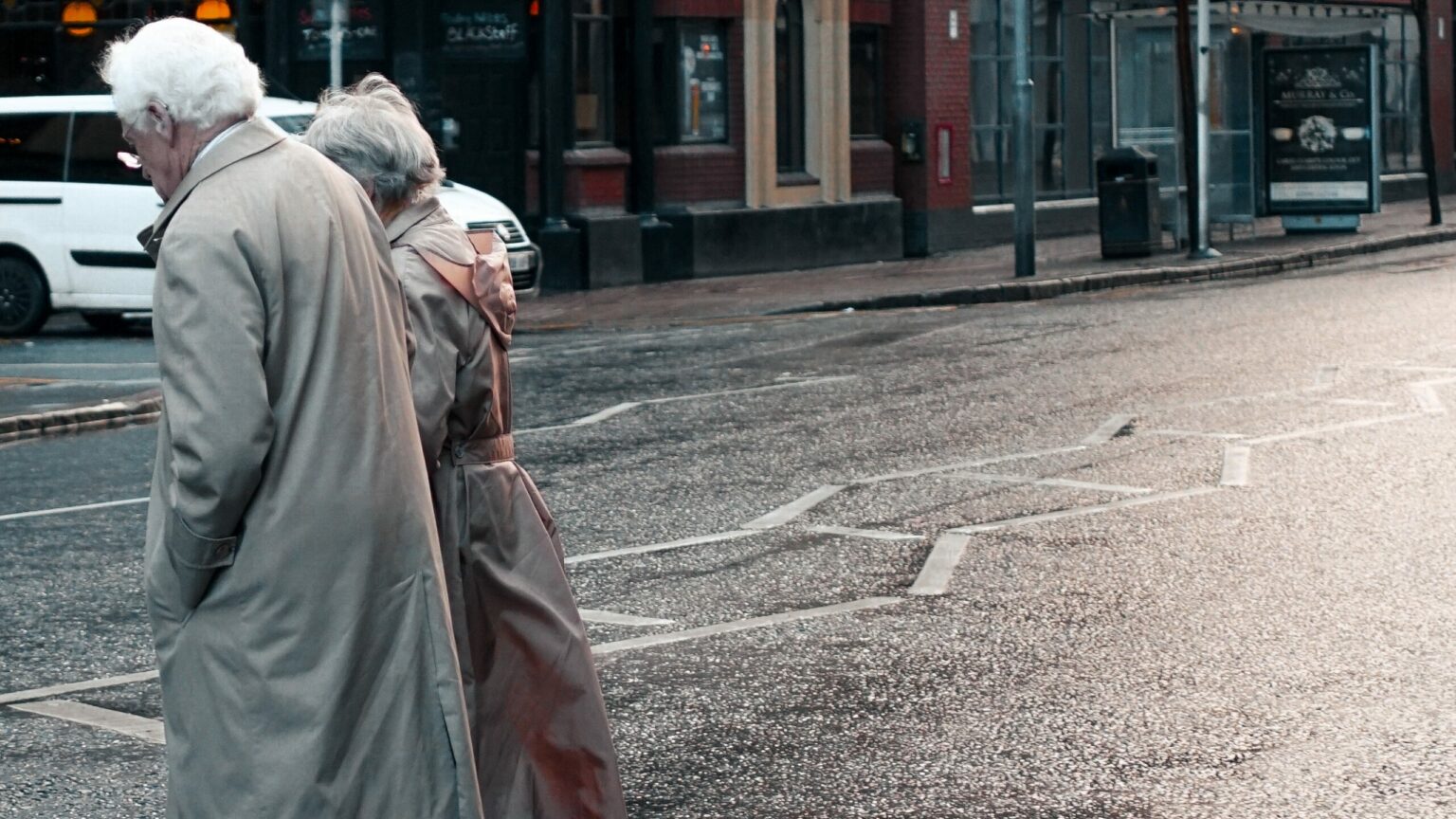 two elderly people crossing a road