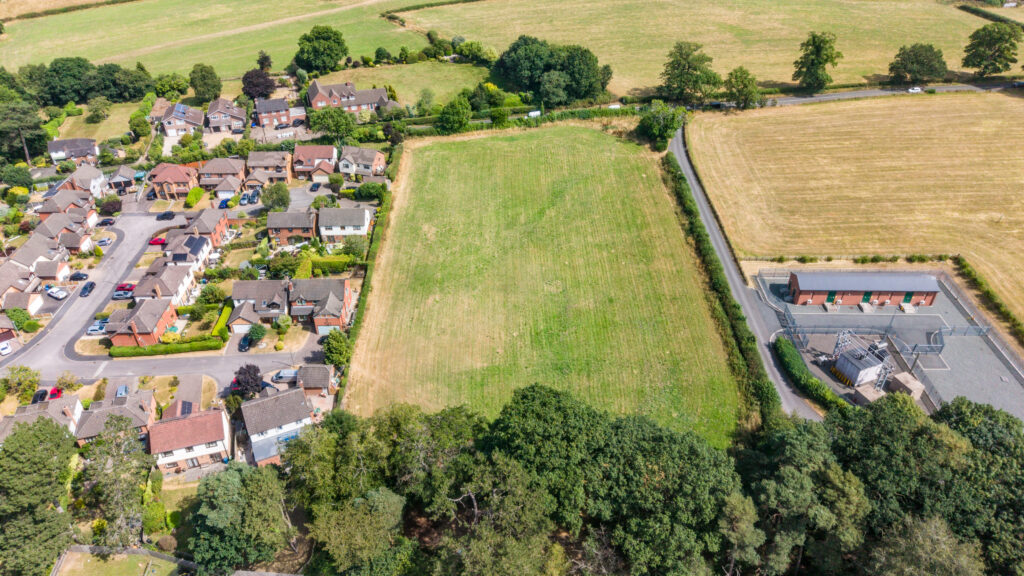 Aerial view of the Cross Butts site, showing the field adjoining existing residential development, established tree cover and surrounding agricultural land.