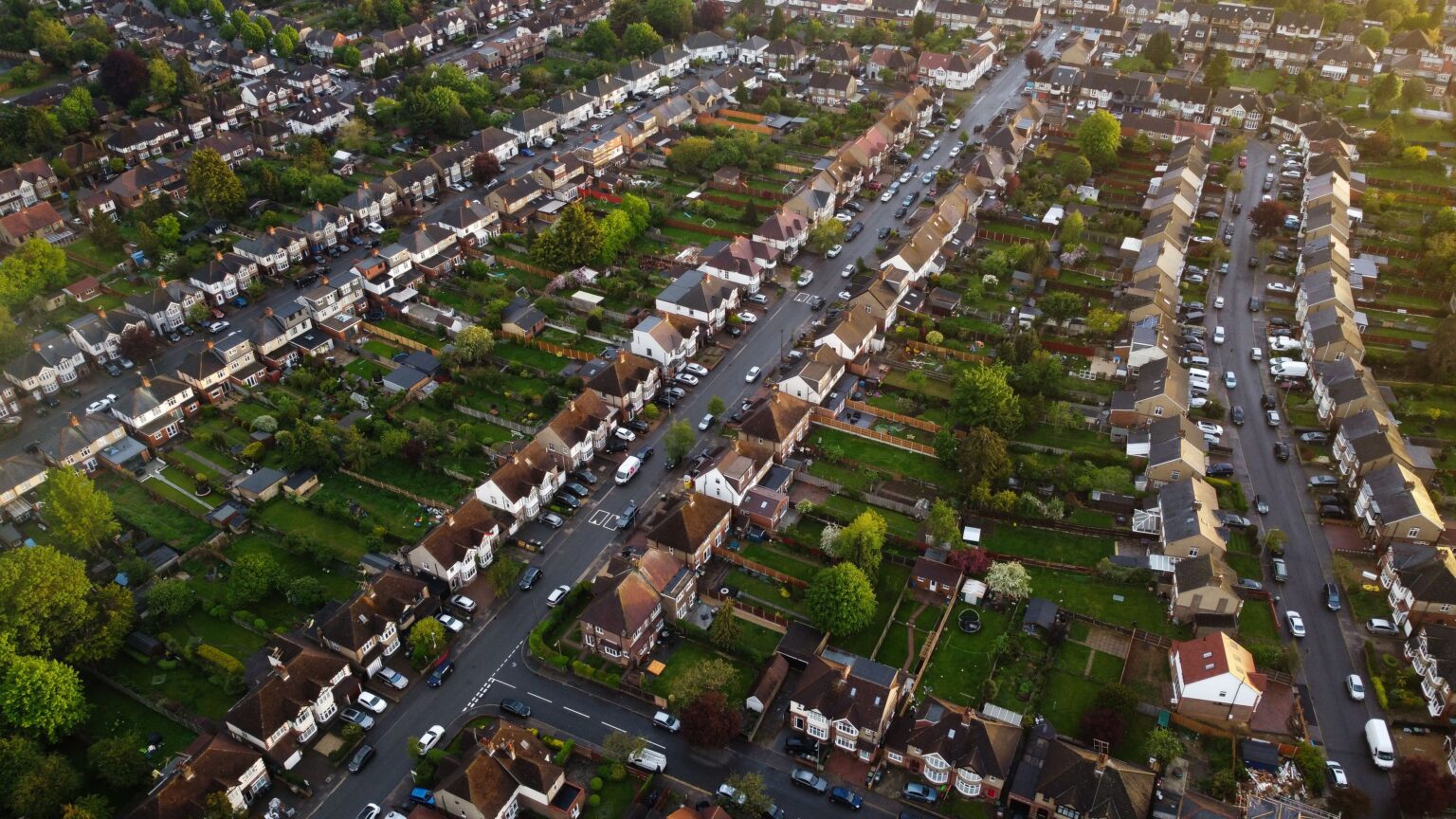 Aerial view of a residential neighbourhood with rows of houses, tree-lined streets and private back gardens.